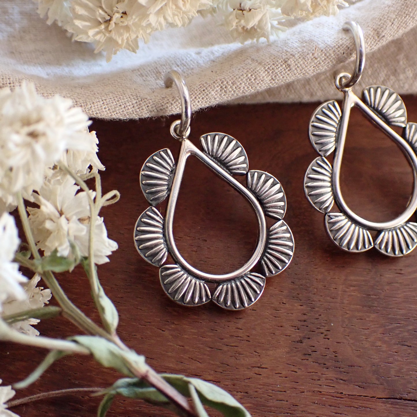 a pair of silver teardrop shaped earrings framed by half round sun ray details