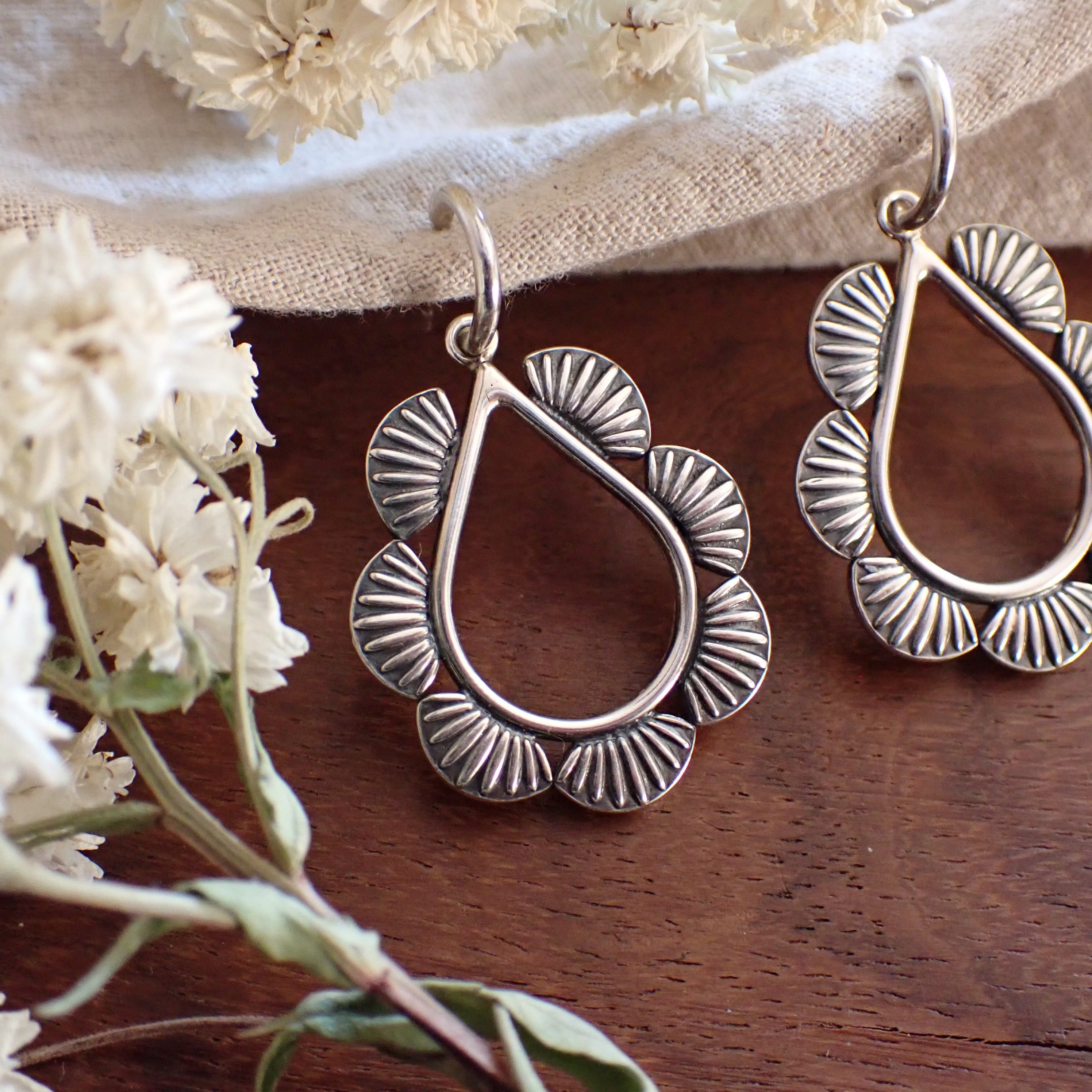 a pair of  silver teardrop shaped earrings framed by half round sun ray details