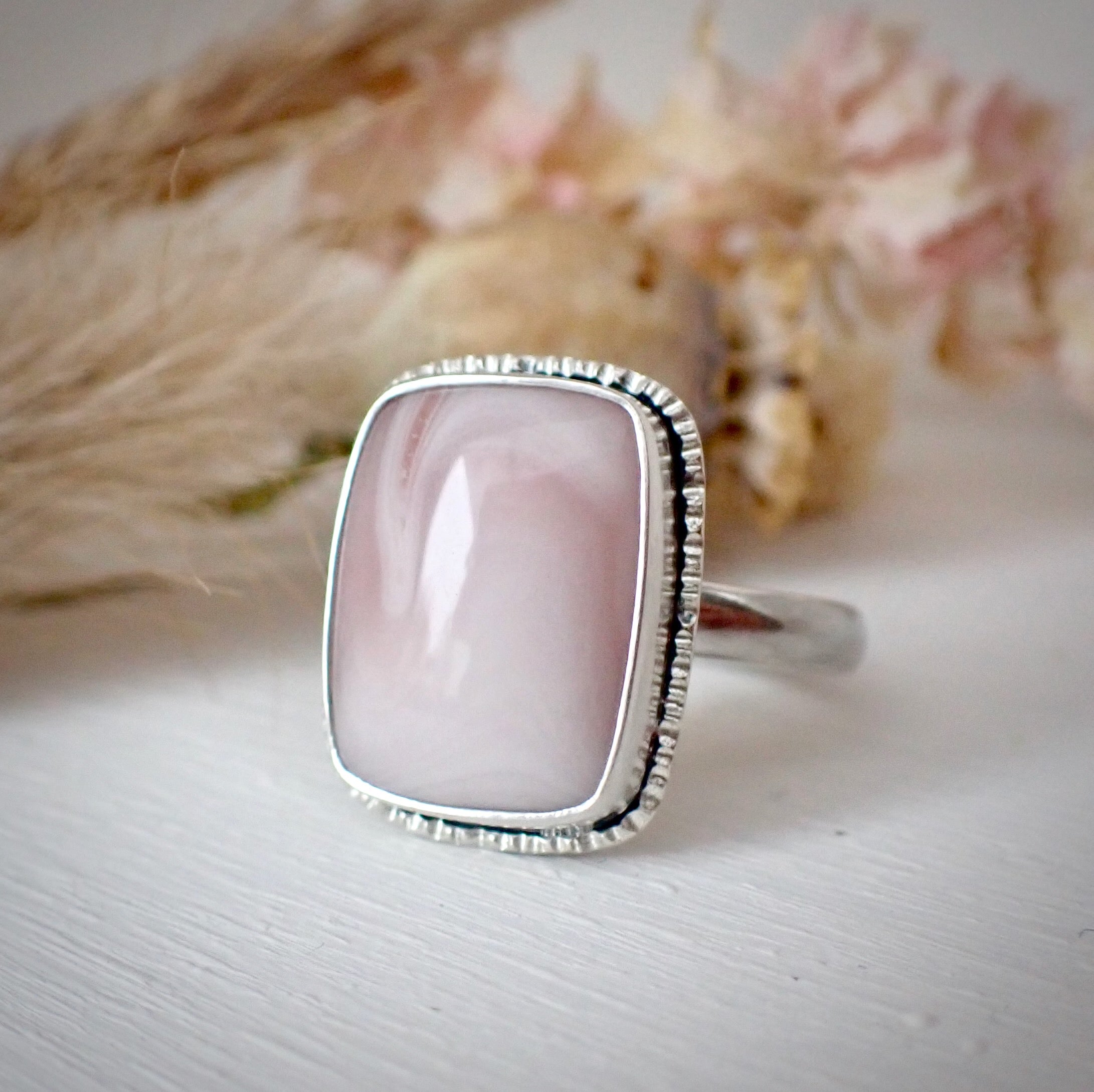 a handmade silver ring featuring a rectangular pale pink jasper, hand carved frame and shadowbox detail