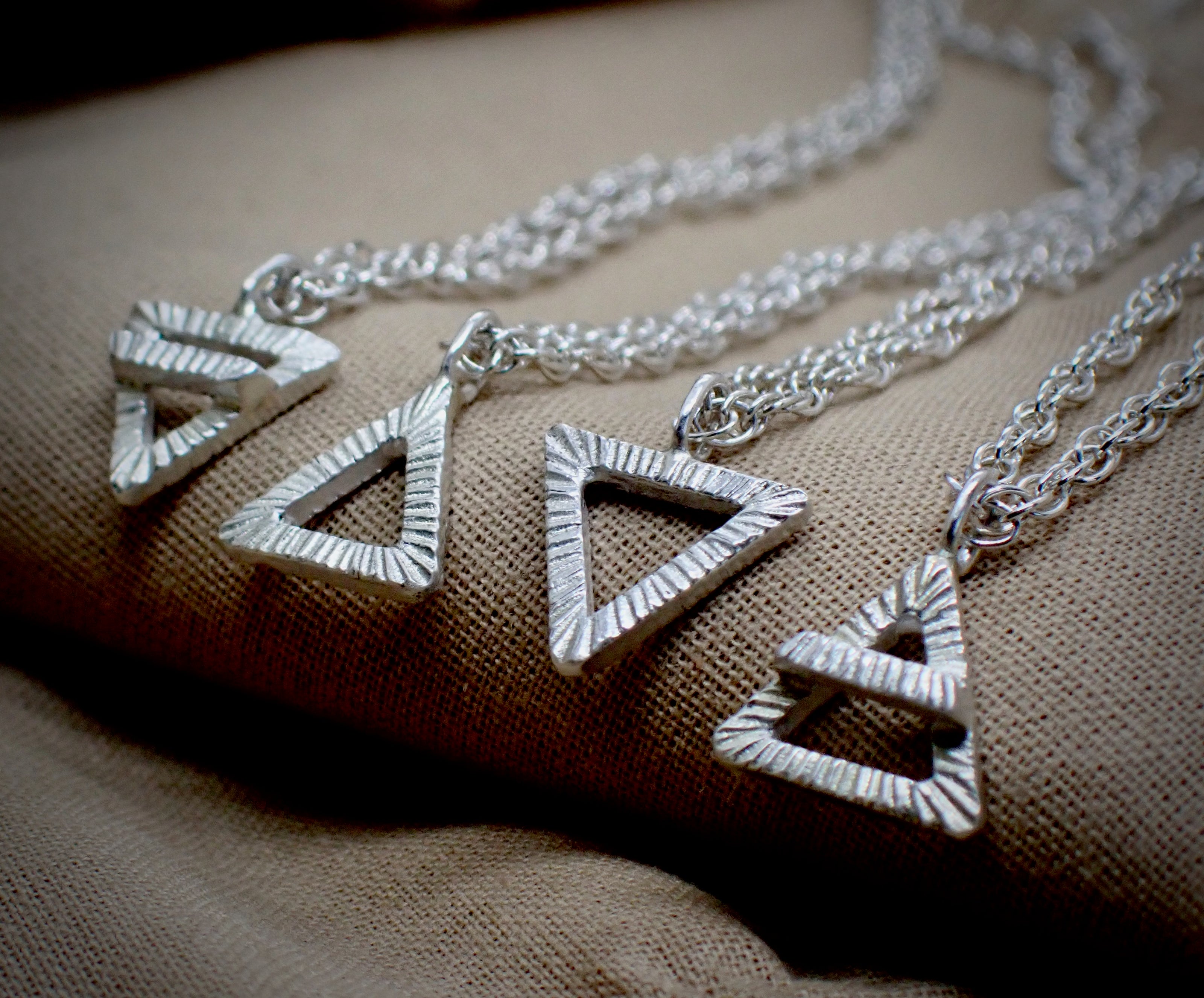 a collection of four hand carved elemental symbol pendants in a row
