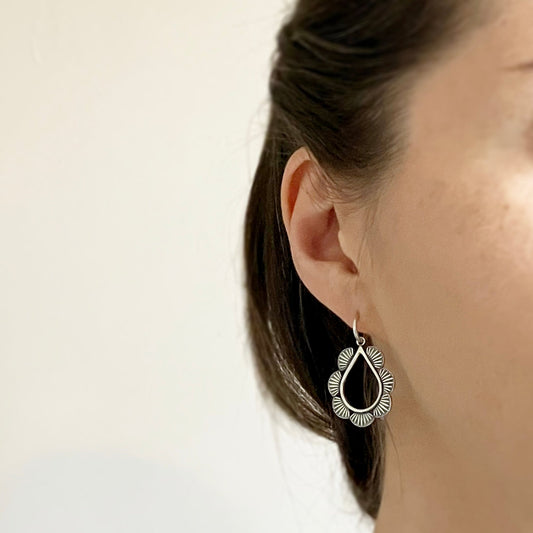 modelled photo to show huggie hoop hugs the earlobe and teardrop design is suspended from this - also shows how the oxidisation lets the detail stand out - styled with hair up, gives a bohemian, relaxed look