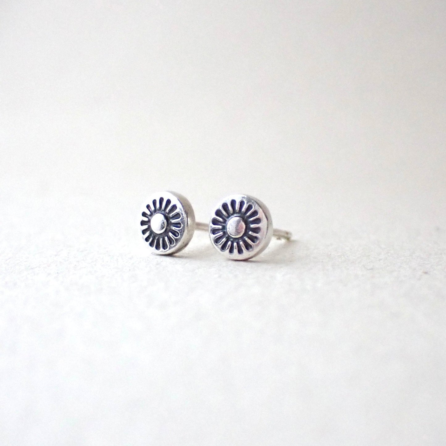 a pair of dinky brightly polished silver earrings featuring a tiny hand stamped sunshine which has been darkened with patina