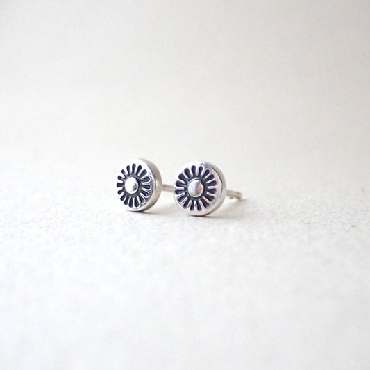 a pair of dinky brightly polished silver earrings featuring a tiny hand stamped sunshine which has been darkened with patina