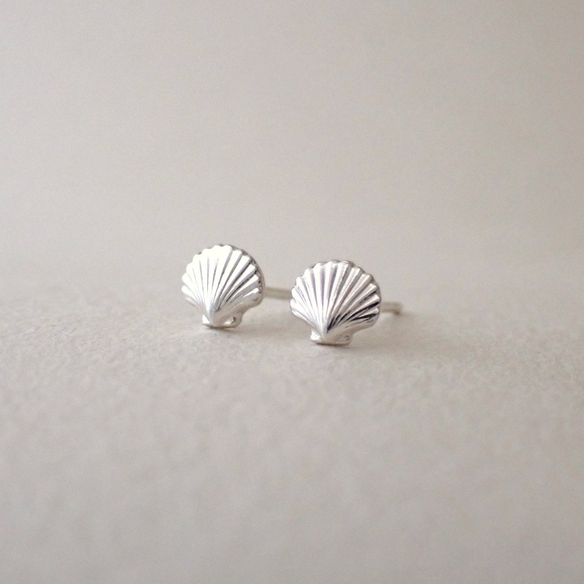 a pair of brightly polished silver scallop shell stud earrings side by side